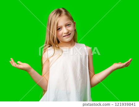 A young girl with long hair in a white dress poses with open arms against green background 121939841