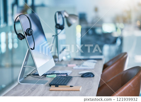 Headphone or headset in an empty call center office with computer monitor display for online customer service or support. Helpdesk hotline assistance gadgets and crm equipment in workplace or station Headphone or headset in an empty call center office with computer monitor display for online customer service or support. Helpdesk hotline assistance gadgets and crm equipment in workplace or station 121939932