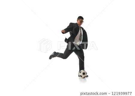 Businessman in suit poised to kick soccer ball with precision, demonstrating focus, energy, and result-driven action against white studio background. Businessman in suit poised to kick soccer ball with precision, demonstrating focus, energy, and result-driven action against white studio background. 121939977