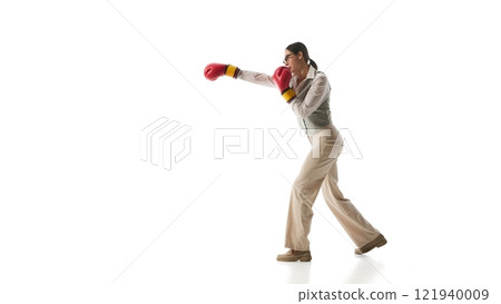 Focused woman in gray vest and beige trousers steps into precise boxing stance, symbolizing determination and adaptability against white studio background. Focused woman in gray vest and beige trousers steps into precise boxing stance, symbolizing determination and adaptability against white studio background. 121940009