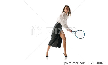 Woman in formal outfit gripping tennis racket mid-action, illustrating fusion of determination and sophistication in professional success against white studio background. 121940028