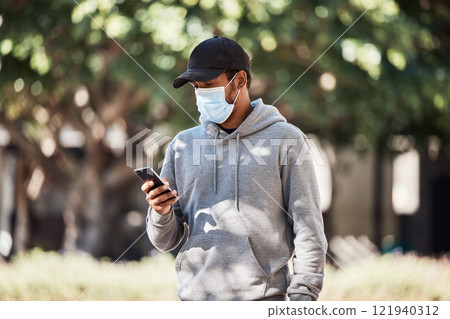 Man looking at phone in nature park, wearing face mask to prevent risk of covid and reading a text message online. Guy standing in garden outside, typing on social media and looking for gps location Man looking at phone in nature park, wearing face mask to prevent risk of covid and reading a text message online. Guy standing in garden outside, typing on social media and looking for gps location 121940312