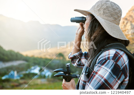 Hiking, exploration and mountain adventure with binoculars, trekking pole and walking aid in a remote landscape with view. Mature woman, hiker and tourist watching birdlife or wildlife in eco nature 121940497