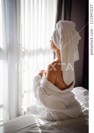 Woman with towel on her head sitting on the bed in the morning 121941037