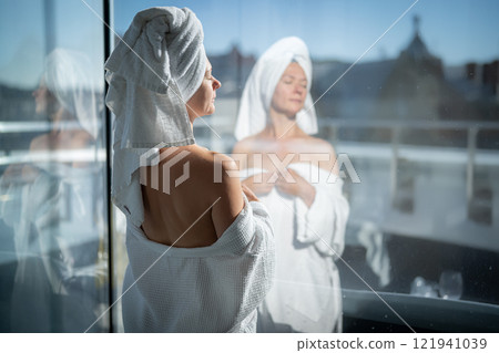 Back view of young woman with towel on her head looking out the window Back view of young woman with towel on her head looking out the window 121941039