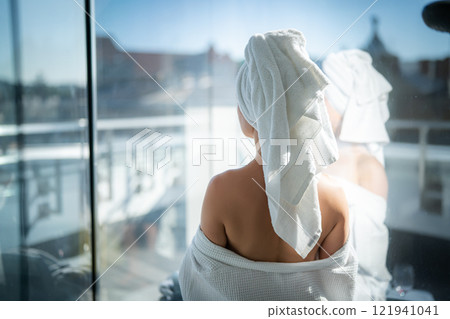 Back view of young woman with towel on her head looking out the window Back view of young woman with towel on her head looking out the window 121941041