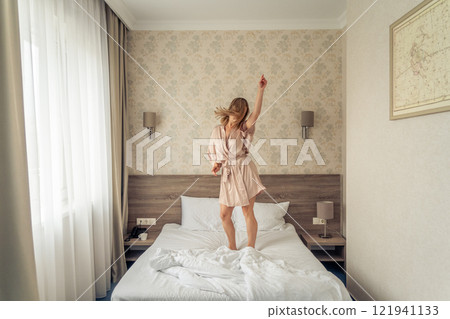 Woman having fun and jumping with bathrobe on bed in hotel room 121941133