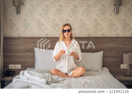 Woman in white bathrobe on sofa and relaxing with cup of coffee at hotel. 121941216