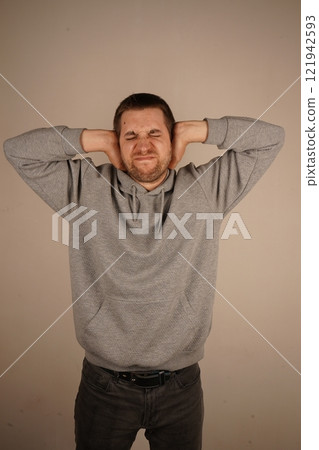 The man firmly presses his palms against his ears, as if trying to block out the noise of the world. His posture suggests a desire to escape from external stress. The man firmly presses his palms against his ears, as if trying to block out the noise of the world. His posture suggests a desire to escape from external stress. 121942593