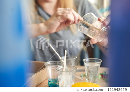 Female adult pouring liquid into clear plastic cups with stirring sticks Female adult pouring liquid into clear plastic cups with stirring sticks 121942659