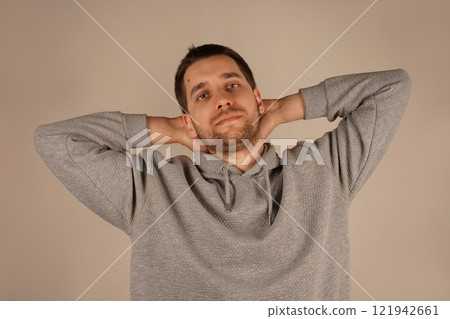 Crossed hands over head. Young guy standing in front of camera with neutral background. Male looking at camera front view. Man in casual clothes. Handsome man. Crossed hands over head. Young guy standing in front of camera with neutral background. Male looking at camera front view. Man in casual clothes. Handsome man. 121942661