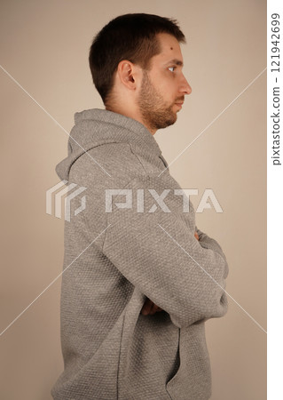 Side view. Handsome guy. Neutral background. Man in casual clothes. Young man standing in front of camera. Male looking at side. Crossed hands. Side view. Handsome guy. Neutral background. Man in casual clothes. Young man standing in front of camera. Male looking at side. Crossed hands. 121942699