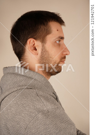 Young man standing in front of camera. Human looking at side. Crossed hands. Side view. Handsome guy. Neutral background. Man in casual clothes. Young man standing in front of camera. Human looking at side. Crossed hands. Side view. Handsome guy. Neutral background. Man in casual clothes. 121942701