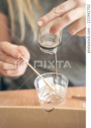 Young caucasian female mixing resin in a cup using a wooden stick for craft Young caucasian female mixing resin in a cup using a wooden stick for craft 121942702