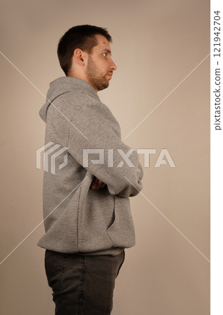 Neutral background. Male in casual clothes. Young man standing in front of camera. Guy looking at side. Crossed hands. Side view. Handsome man. 121942704