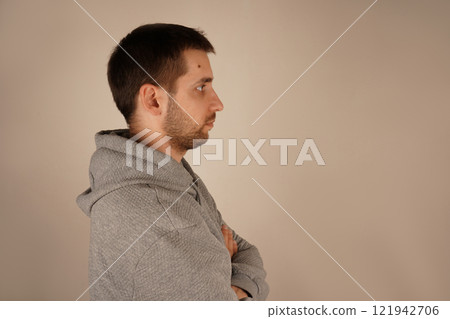 Male looking at side. Crossed hands. Side view. Handsome man. Young guy standing in front of camera. Neutral background. Man in casual clothes. 121942706