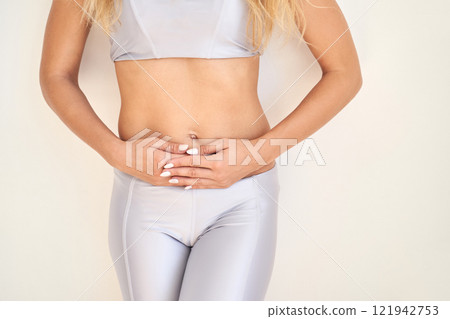 Caucasian young female in athletic wear holding stomach in discomfort against Caucasian young female in athletic wear holding stomach in discomfort against 121942753