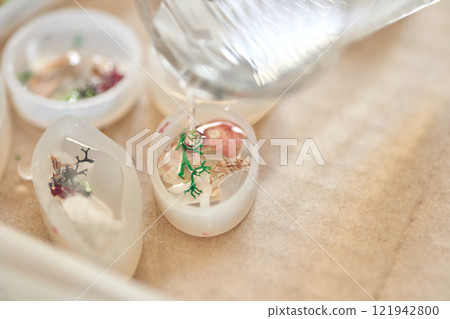 Crafting resin art with dried flowers and shells in molds on beige surface 121942800