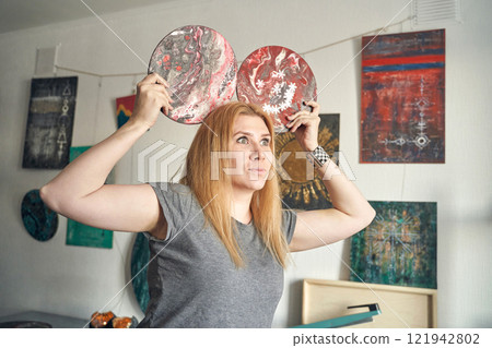 Caucasian female adult artist holding abstract paintings in studio with colorful Caucasian female adult artist holding abstract paintings in studio with colorful 121942802