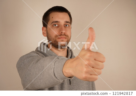 Okay sign. Agree. Charming confident guy dressed gray hoodie showing thumb up alone. Young handsome man with beard over isolated gray background giving a thumbs up gesture. Okay sign. Agree. Charming confident guy dressed gray hoodie showing thumb up alone. Young handsome man with beard over isolated gray background giving a thumbs up gesture. 121942817