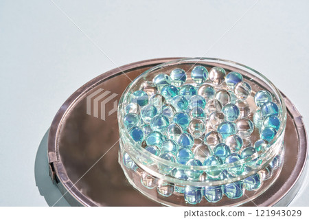 Glass marbles in transparent dish on metal tray with light blue background 121943029