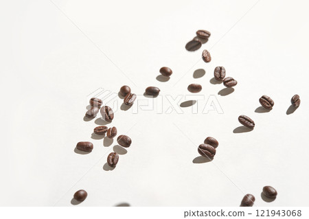 Scattered coffee beans on white surface with shadows highlighting their texture Scattered coffee beans on white surface with shadows highlighting their texture 121943068