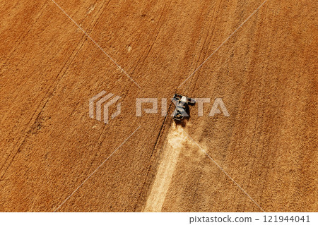 Harvesting of grain in summer. Drone aerial view of harvester working in field. Combine harvester agricultural machine collecting golden ripe wheat or rye on field. View from above. Copy space Harvesting of grain in summer. Drone aerial view of harvester working in field. Combine harvester agricultural machine collecting golden ripe wheat or rye on field. View from above. Copy space 121944041