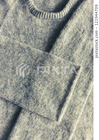 Grey melange knitting sweater with i-cord bind off. Mix of grey wool and white cashmere. Knitting pattern background. Knitting lifestyle. Cozy hobby. Warm knitwear. Craft product concept. Grey melange knitting sweater with i-cord bind off. Mix of grey wool and white cashmere. Knitting pattern background. Knitting lifestyle. Cozy hobby. Warm knitwear. Craft product concept. 121944709