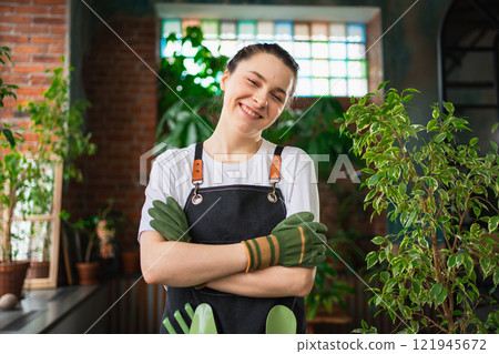 Running of own business. Young woman florist wearing apron in botanical store with green plants. Happy small business owner working at flower shop standing surrounded by plants. Small business 121945672