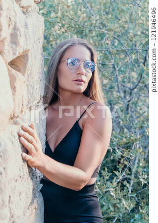 Woman Sunglasses Rock Formation - A woman wearing sunglasses stands next to a rock formation in a natural outdoor setting. 121946496