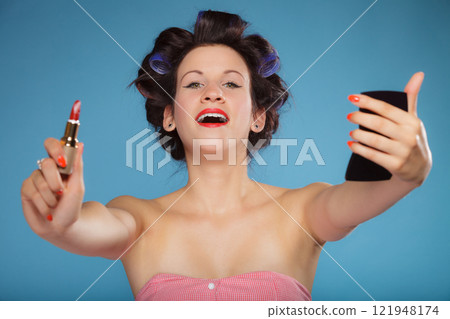 Girl in hair curlers applying red lipstick 121948174