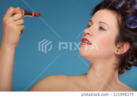 Girl in hair curlers applying red lipstick 121948175