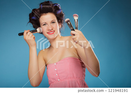 woman in hair rollers holds makeup brushes 121948191