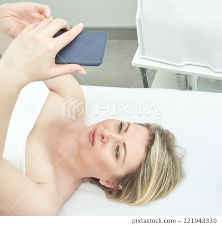 Caucasian adult female taking a selfie on a smartphone while lying down in a spa Caucasian adult female taking a selfie on a smartphone while lying down in a spa 121948330