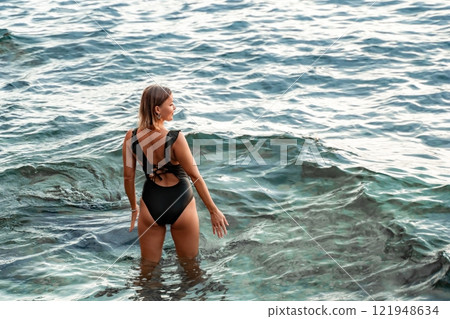 Woman Swimsuit Ocean Water - Woman in a black swimsuit wading in the ocean water. 121948634