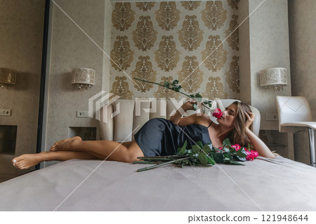 A woman is laying on a bed with a bouquet of red roses in her lap. Concept of romance and intimacy, as the woman is surrounded by the flowers and he is in a relaxed and comfortable position. A woman is laying on a bed with a bouquet of red roses in her lap. Concept of romance and intimacy, as the woman is surrounded by the flowers and he is in a relaxed and comfortable position. 121948644