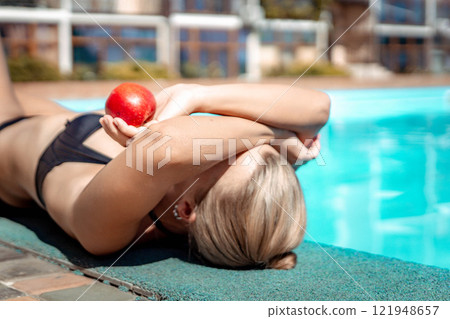 Bikini-clad woman enjoys poolside relaxation. Poolside ambiance. Capturing woman's relaxed time near pool. 121948657