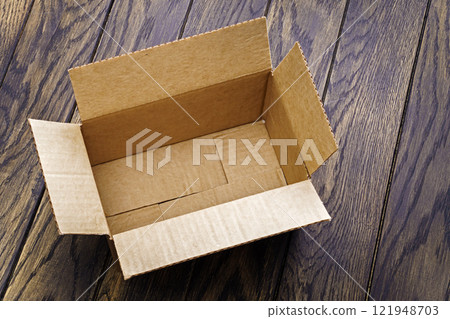 Open brown cardboard box sitting on wooden table 121948703
