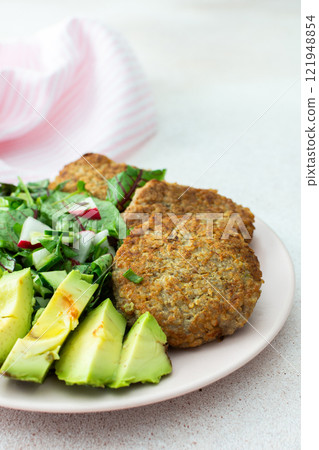 Quinoa cutlets and mixed salad with avocado and radishes, kiwi and water Quinoa cutlets and mixed salad with avocado and radishes, kiwi and water 121948854