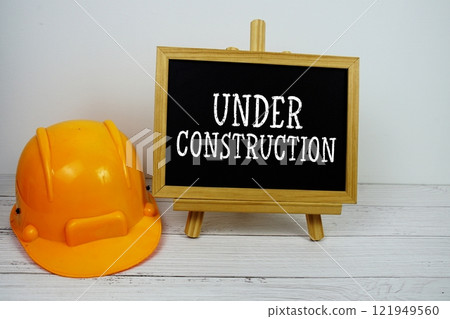 Under Construction text on blackboard with safety helmet on wooden background 121949560