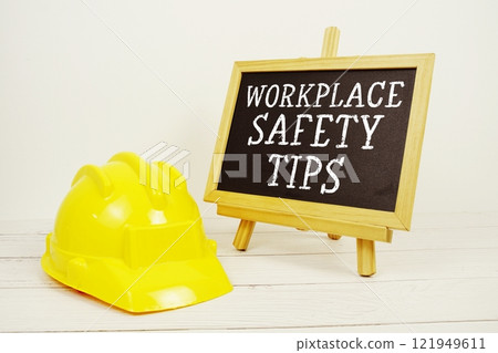 Workplace Safety Tips text on blackboard with safety helmet on wooden background 121949611