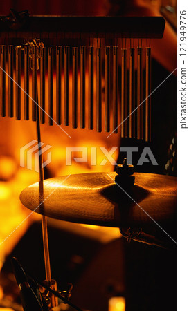 Close-up of a drum set with a cymbal and chimes in the foreground. The background is blurred and orange 121949776