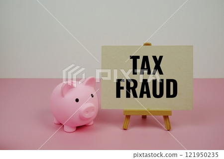 Tax Fraud quotes text on paper card and easel standing with piggy saving on pink background Tax Fraud quotes text on paper card and easel standing with piggy saving on pink background 121950235