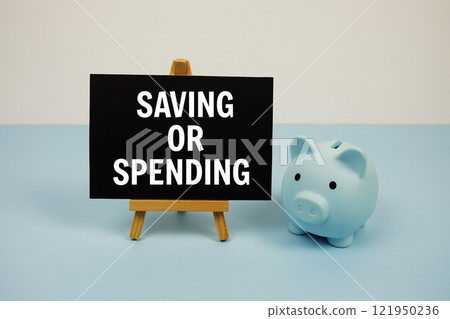 Saving or Spending text on paper card and easel standing with piggy saving on blue background Saving or Spending text on paper card and easel standing with piggy saving on blue background 121950236