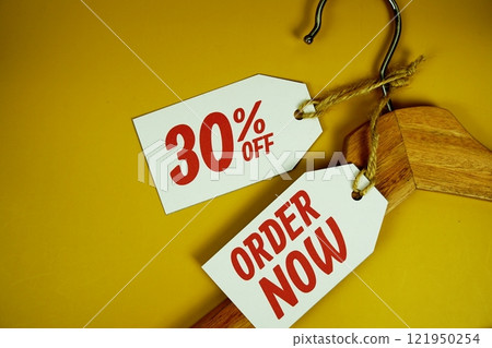 Order Now and Sale 30% on price tag with wooden clothes hanger top view on yellow background 121950254