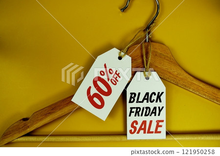 Black Friday and Sale 60% on price tag with wooden clothes hanger top view on yellow background 121950258