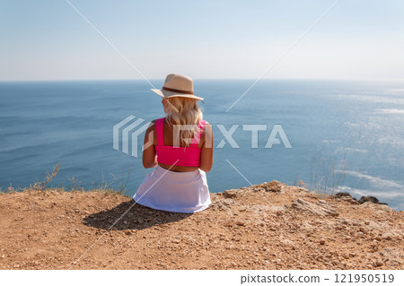 A woman in a pink top and white skirt sits on a beach, looking out at the ocean. A woman in a pink top and white skirt sits on a beach, looking out at the ocean. 121950519