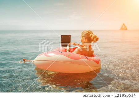 Woman laptop sea. Freelancer woman in sunglases floating on an inflatable big pink donut with a laptop in the sea. People summer vacation rest lifestyle concept 121950534