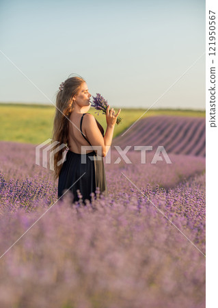 woman stands in a lavender field of purple flowers, holding a bouquet of flowers. The scene is serene and peaceful, with the woman taking a moment to enjoy the beauty of nature. woman stands in a lavender field of purple flowers, holding a bouquet of flowers. The scene is serene and peaceful, with the woman taking a moment to enjoy the beauty of nature. 121950567