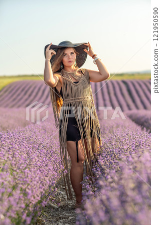 A woman is standing in a field of purple flowers, wearing a black dress and a black hat. 121950590